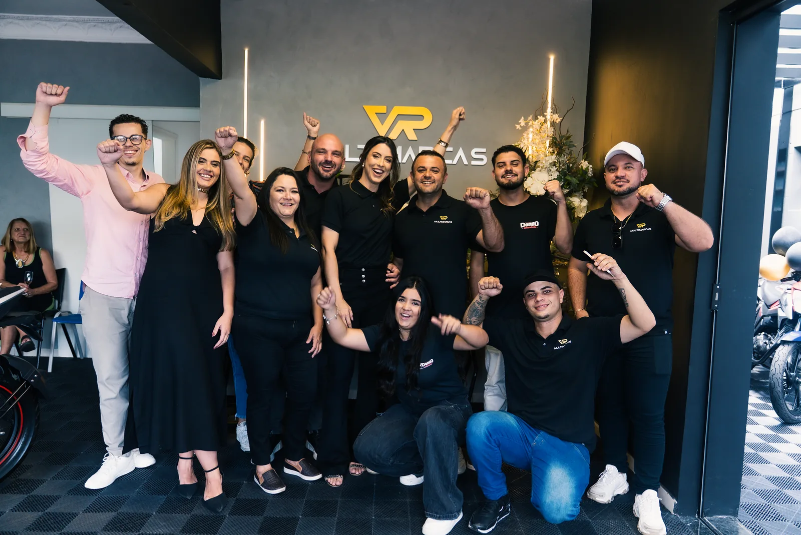 Equipe da VR Multimarcas Santa Rita do Sapucaí comemorando na frente do logo, no dia da inauguração